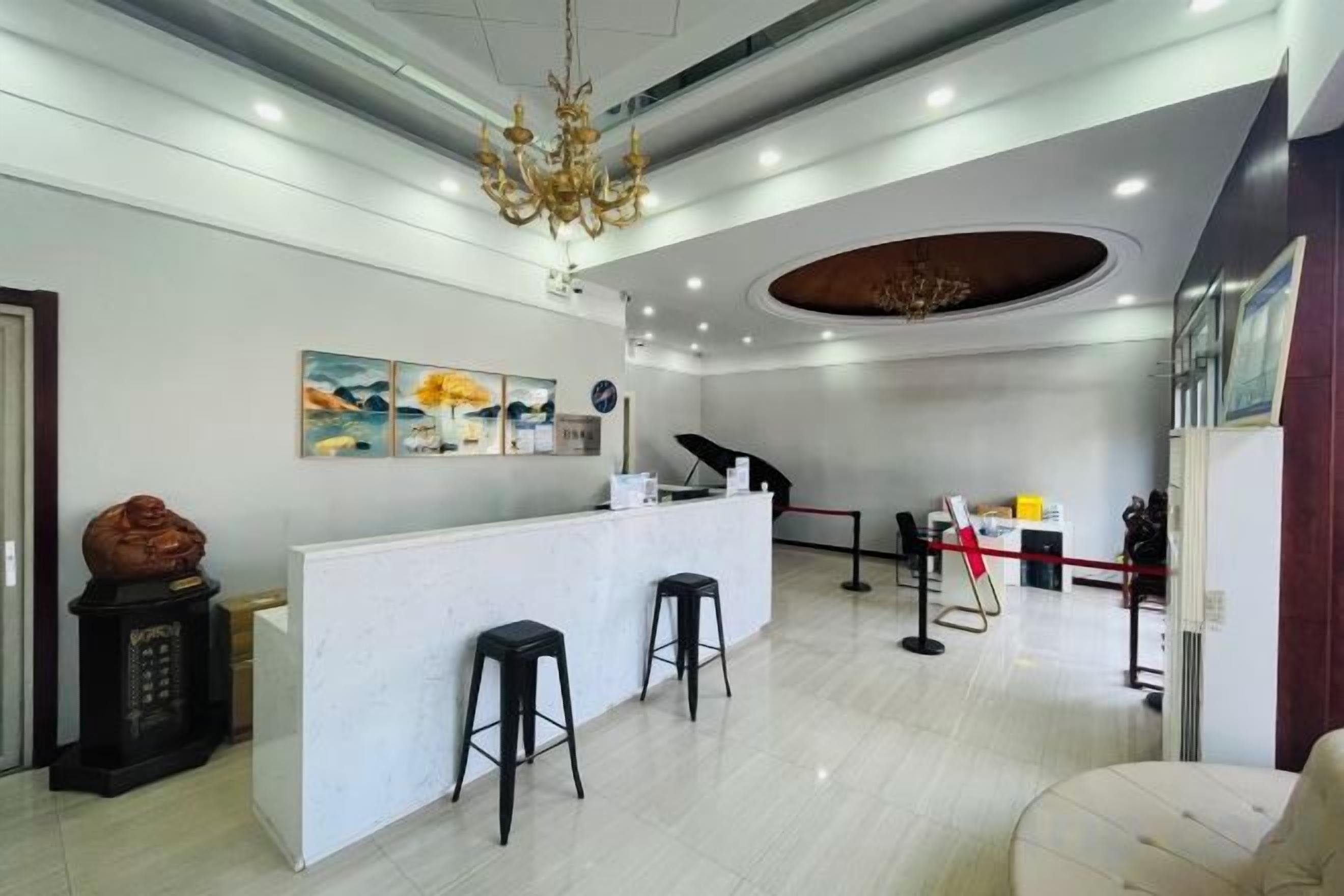 A reception area with a white counter, two black bar stools, a chandelier, and a painting on the wall.