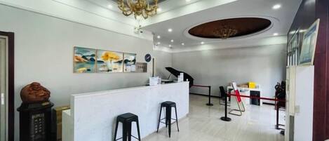 A reception area with a white counter, two black bar stools, a chandelier, and a painting on the wall.