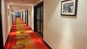Un couloir d’hôtel avec un tapis rouge, des œuvres d’art encadrées accrochées au mur et une porte sur la droite.