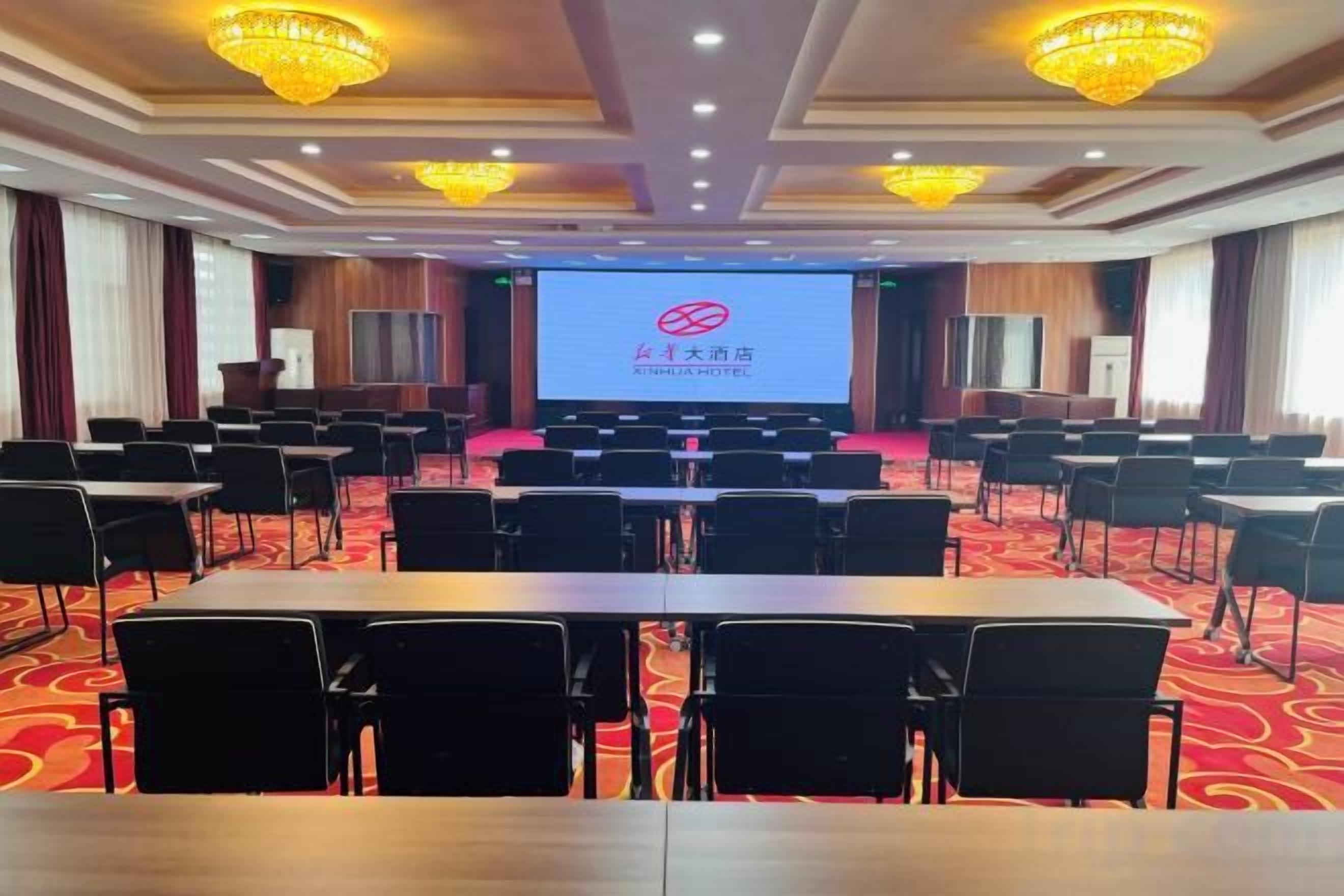 A conference room with a stage, multiple rows of chairs, and a large screen displaying a logo.