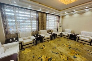 Une chambre d’hôtel dotée d’une grande moquette, de plusieurs coins salon et d’une grande fenêtre avec des rideaux.