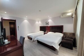 Een hotelkamer met twee bedden, een bureau met stoel, een televisie en een airconditioning.