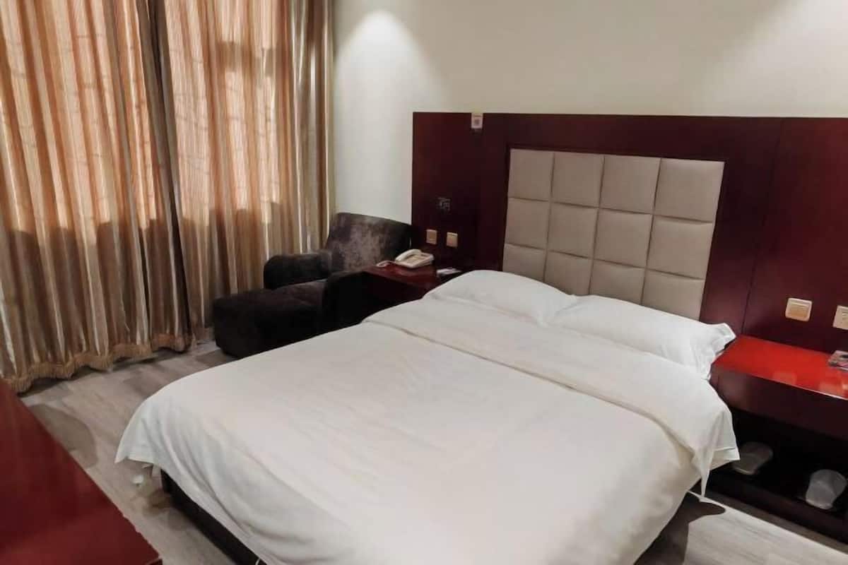 Habitación de hotel con una cama, una silla, una mesita de noche con un teléfono y una mesita auxiliar roja.