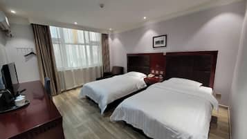 A hotel room with two beds, a desk with a computer, a chair, and a window with curtains.