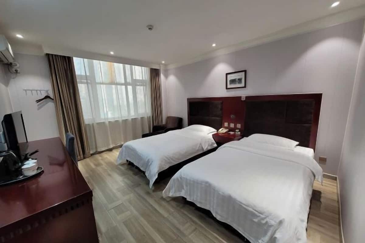 Una habitación de hotel con dos camas, un escritorio con computadora y una ventana con cortinas.