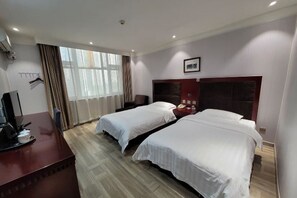 Una habitación de hotel con dos camas, un escritorio con computadora y una ventana con cortinas.