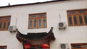 A traditional building with a tiled roof, multiple windows with wooden frames, and air conditioning units. - Xuancheng Airitang Inn (Jing County)