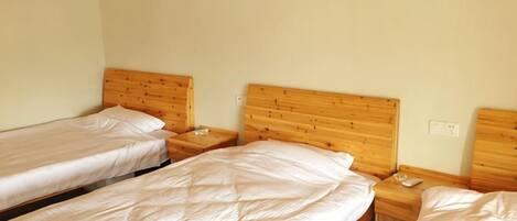 A room with three single beds, wooden headboards, and bedside tables with lamps.