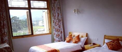 Habitación con dos camas, un escritorio y una silla. Se ve una ventana con cortinas.