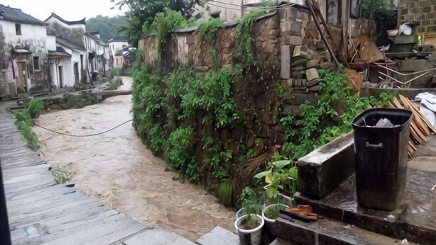 A narrow alley with a stone wall covered in greenery, a wooden staircase, and a trash bin. - Xuancheng Airitang Inn (Jing County)