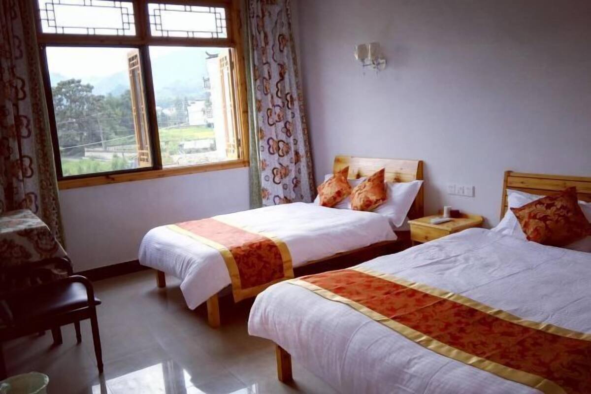 Une chambre avec deux lits, une chaise, une fenêtre avec des rideaux et une vue sur l’extérieur.