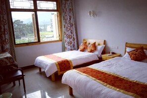 Una habitación con dos camas, una silla, un ventanal con cortinas y vistas al exterior.