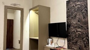A modern room with a built-in wardrobe, a flat-screen TV mounted on the wall, and a marble-patterned accent wall. - Sri Madhav Stay (Varanasi)