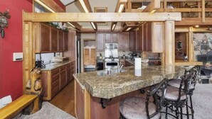 Een keuken met houten balken, granieten aanrechtbladen en een centraal eiland met barstoelen.