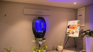 Zona de spa con un cartel de prohibido fumar, un elemento acuático iluminado en azul, plantas en macetas y un cartel promocional de 'Feathers Spa'.