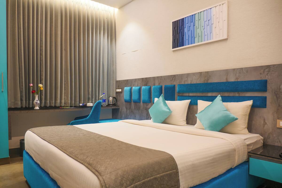 A modern hotel room with a large bed, a desk with a chair, a vase with flowers, and a painting on the wall.