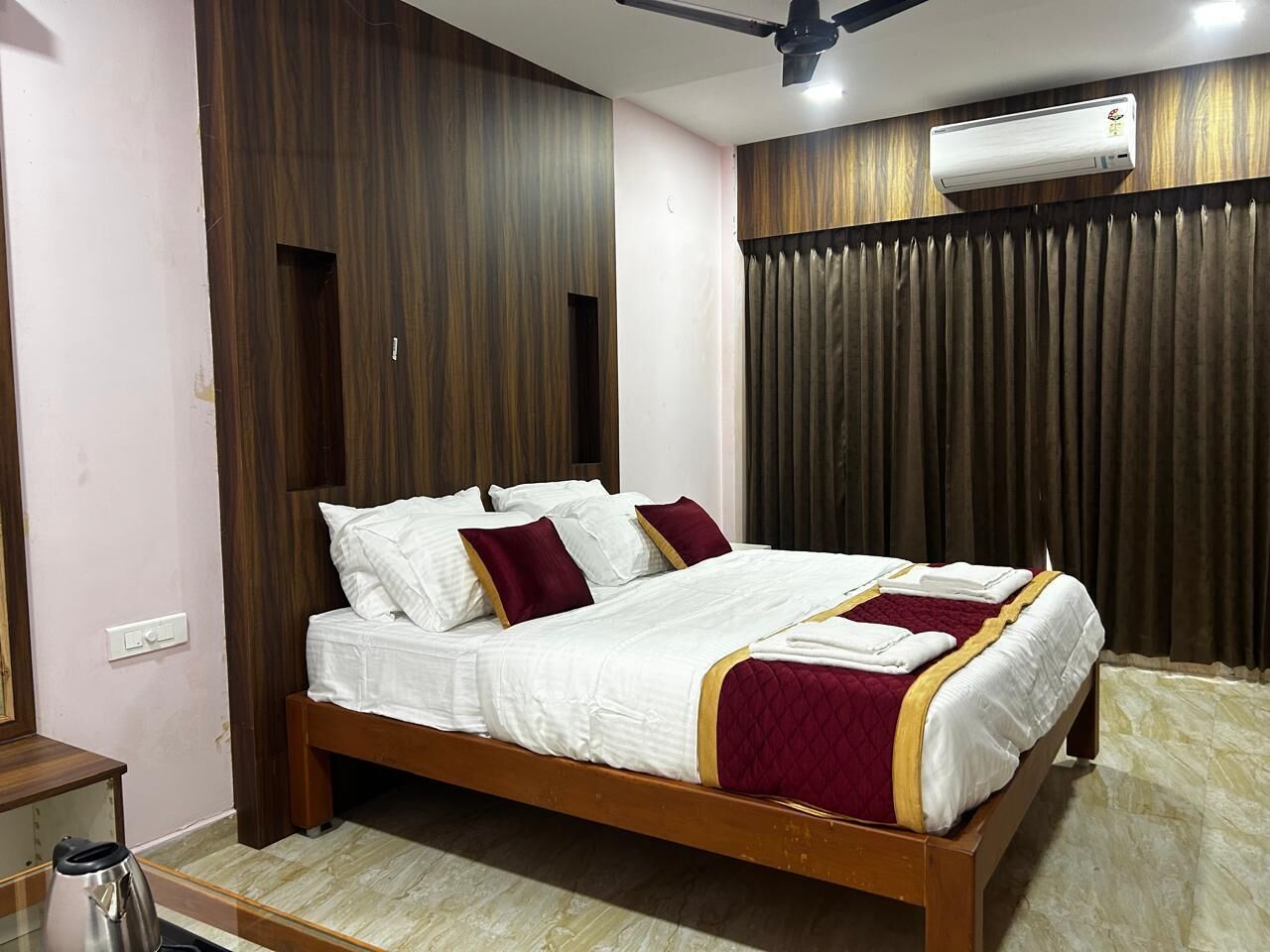 A neatly made bed with white linens and maroon pillows, a wooden headboard, and a large air conditioning unit above it.