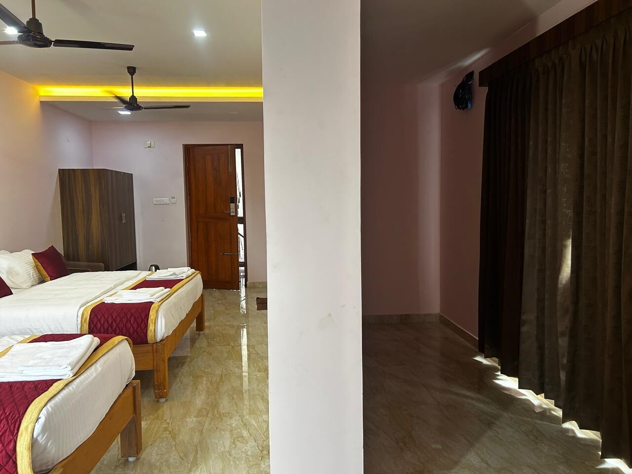 A hotel room with three beds, a wooden wardrobe, a ceiling fan, and a large window with curtains.