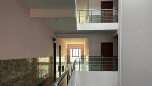 A multi-level interior with a glass railing, a marble wall, and a corridor leading to a door. - J V Residency (Salem)