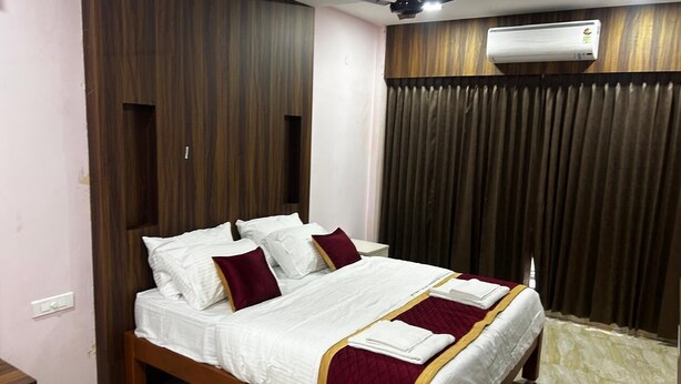 A neatly made bed with white linens and maroon accents, a ceiling fan, and an air conditioning unit. - J V Residency (Salem)