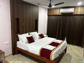 A neatly made bed with white linens and maroon accents, a ceiling fan, and an air conditioning unit. - J V Residency (Salem)