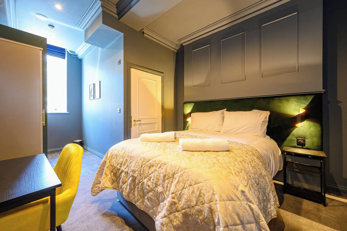 A hotel room with a bed, a desk, a chair, and a nightstand.
