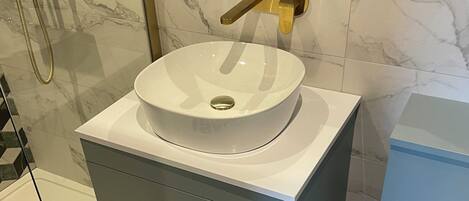 Un baño con lavamanos blanco, grifo dorado y pared de azulejos de mármol.