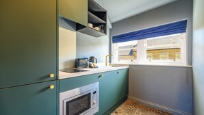 Una cocina con armarios color turquesa, un microondas y una ventana con cortina azul.