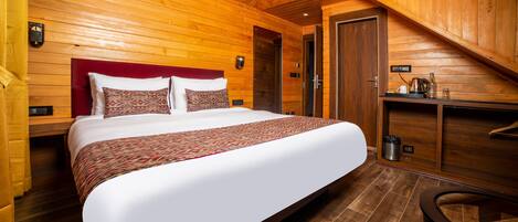 A wooden-paneled room with a large bed, a desk, and a door.