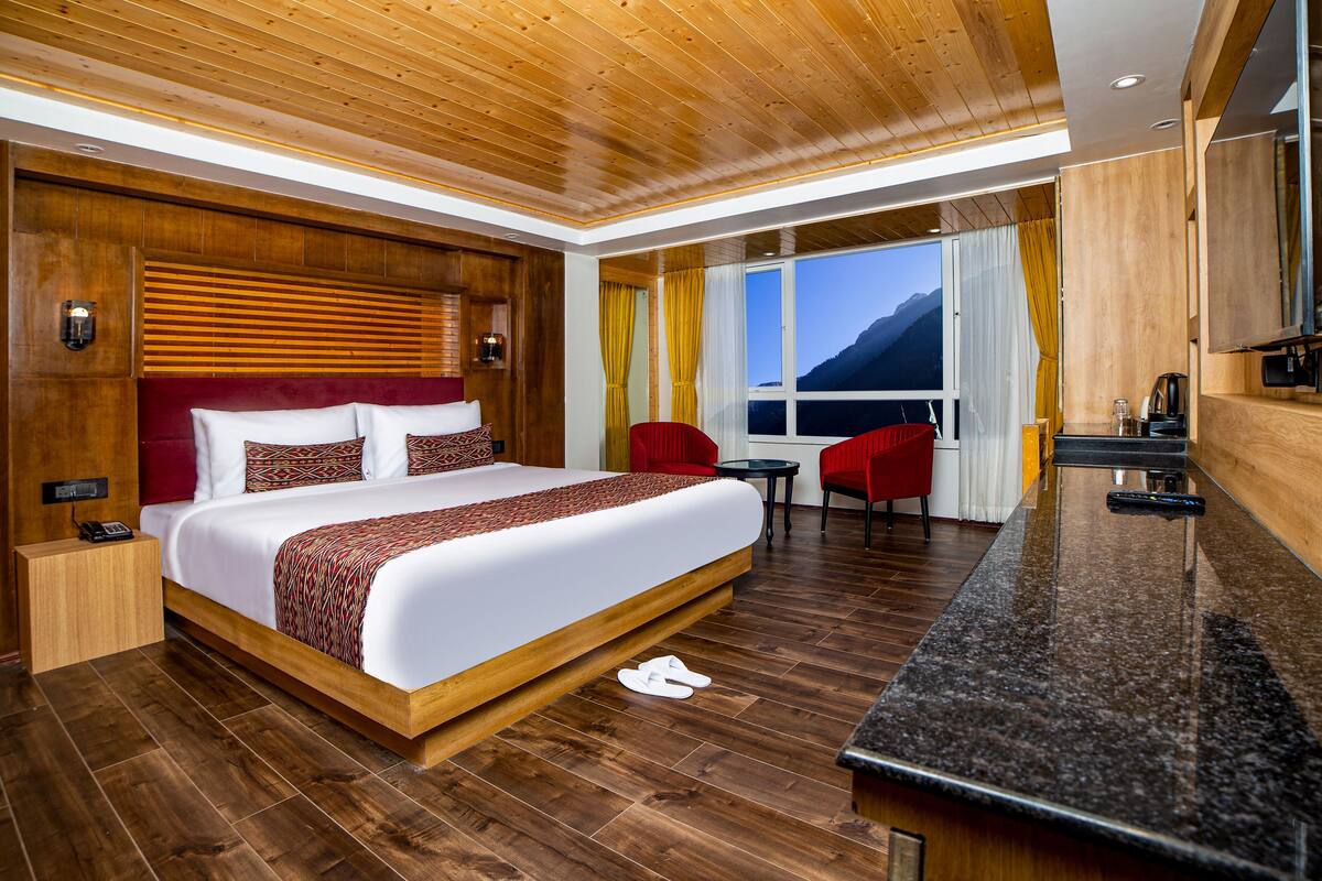 A modern hotel room with a large bed, wooden headboard, and a view of mountains through the window.