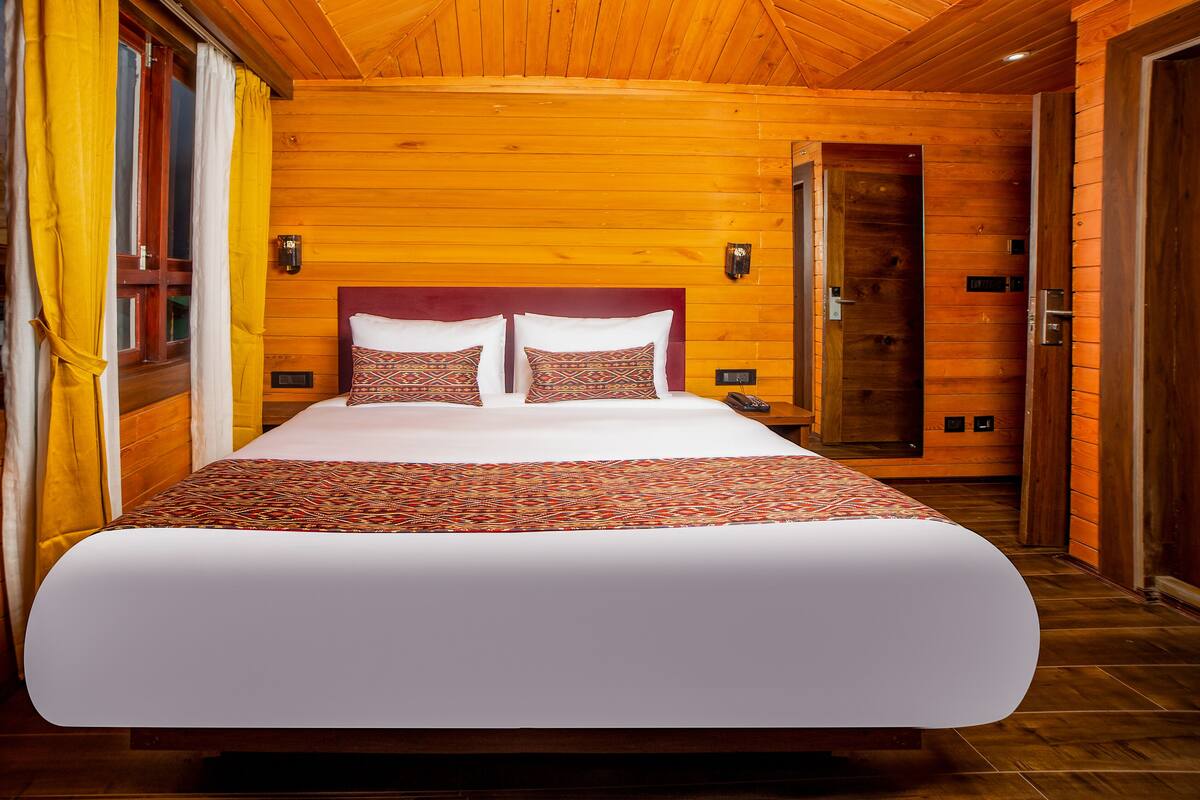 A large bed with patterned bedding in a wooden room with a wooden ceiling and walls.
