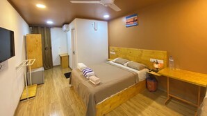 A bedroom with a bed, a wooden headboard, a nightstand, a ceiling fan, and a painting on the wall. - Ever Blue Guest House (Mathiveri)