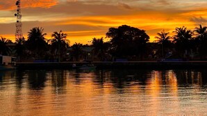 A sunset over a calm body of water with palm trees and a communication tower in the background. - Ever Blue Guest House (Mathiveri)