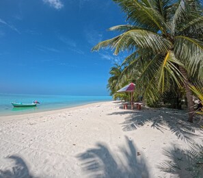 Une plage de sable blanc, un ciel bleu azur et un bateau vert sur l’eau.