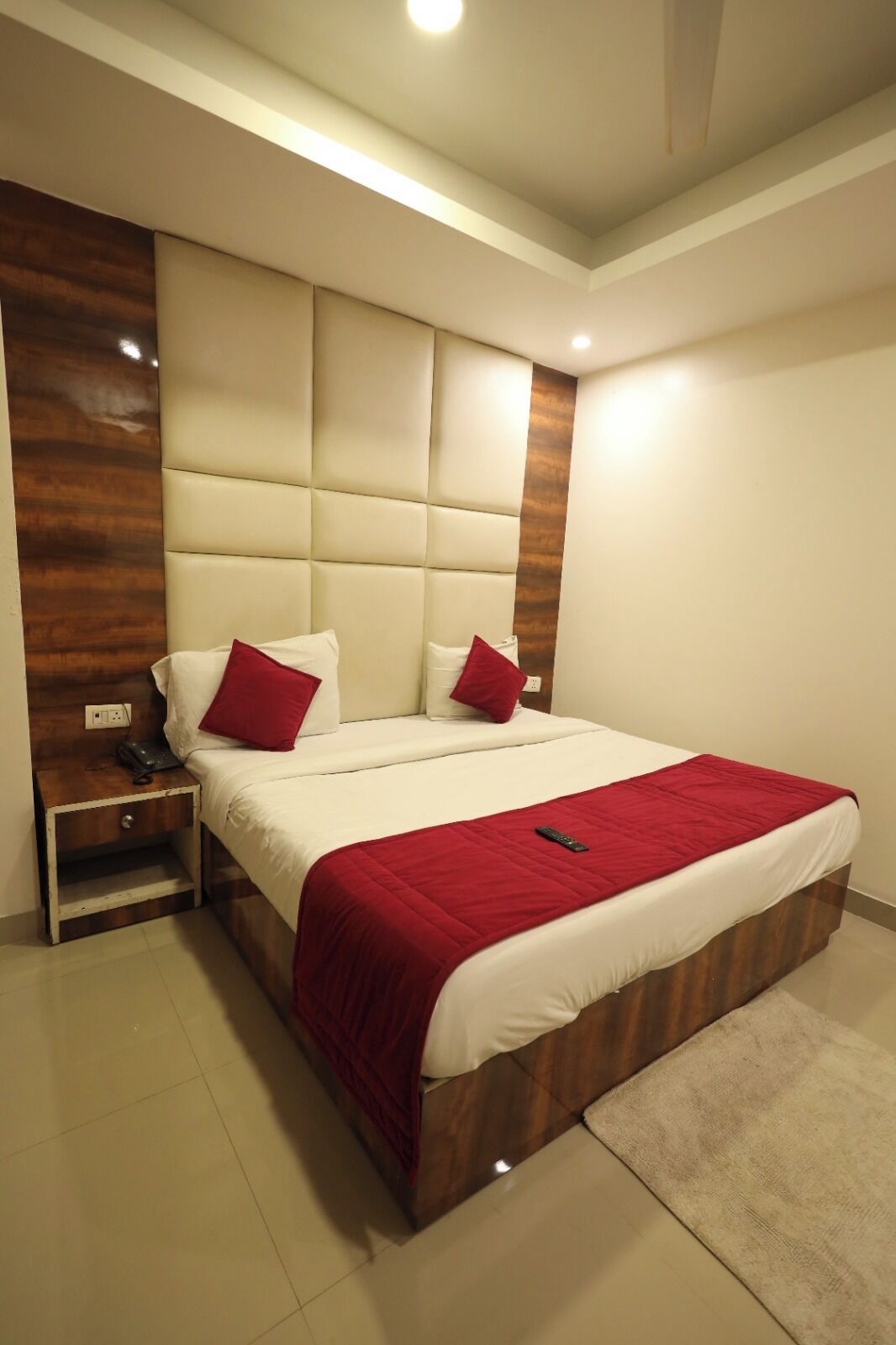 Une chambre moderne avec un grand lit, deux tables de chevet, un mur d’accent en bois et un luminaire au plafond.
