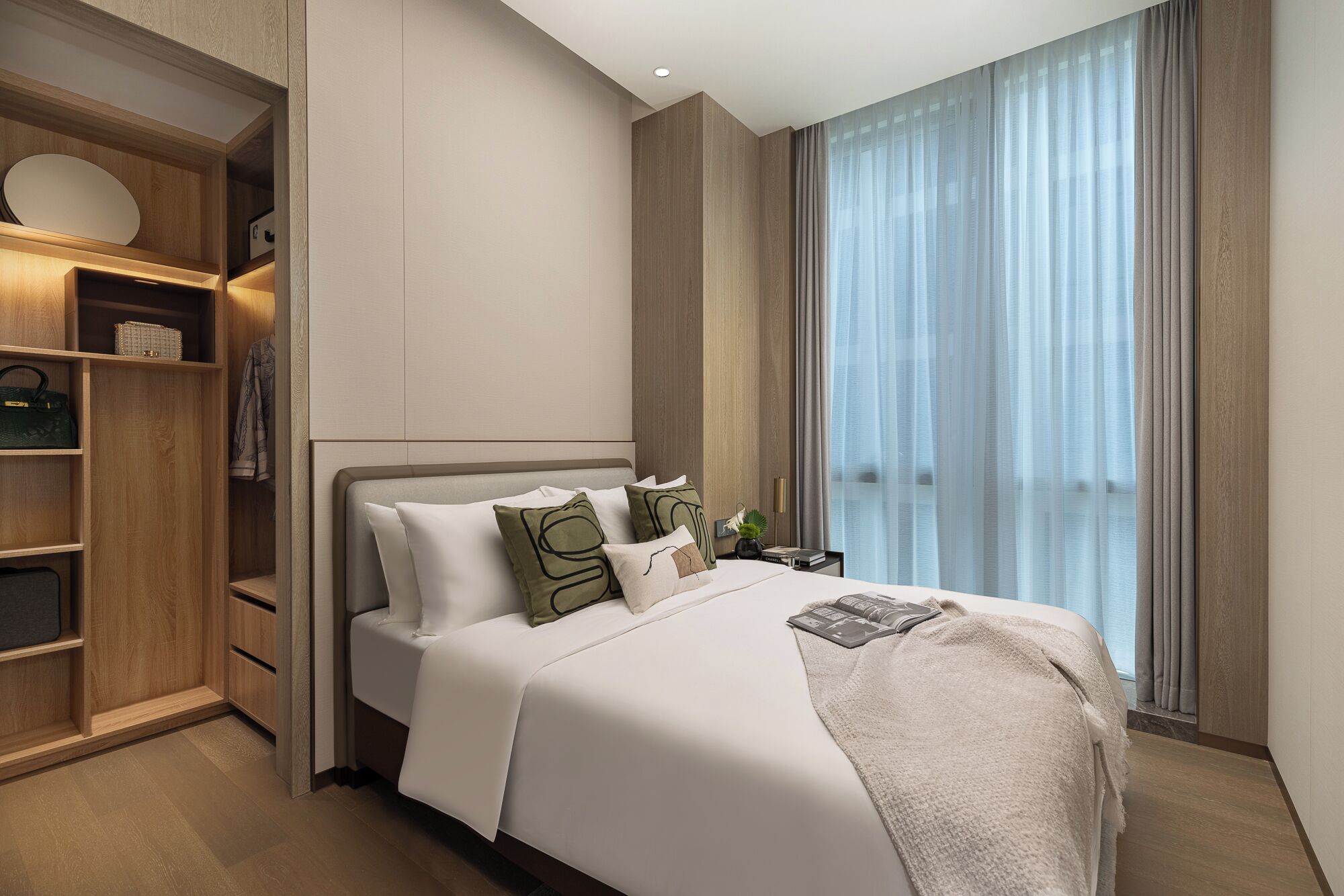 A modern hotel room with a large bed, a built-in wardrobe, and a large window with curtains.