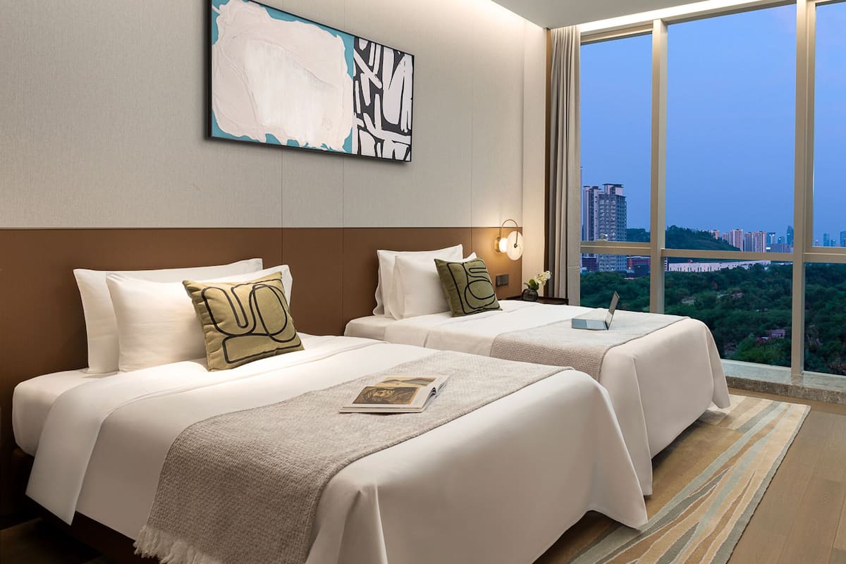 A hotel room with two beds, a large window, and a city view.