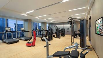 Une salle de sport moderne équipée de tapis de course, d’appareils de musculation et d’un vélo d’exercice rouge.