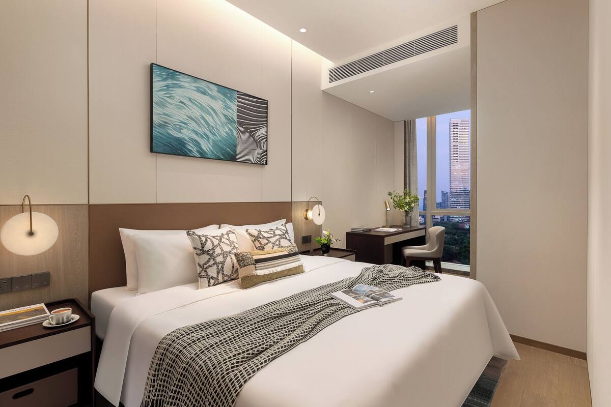 A modern hotel room with a large bed, a desk, and a view of the cityscape.