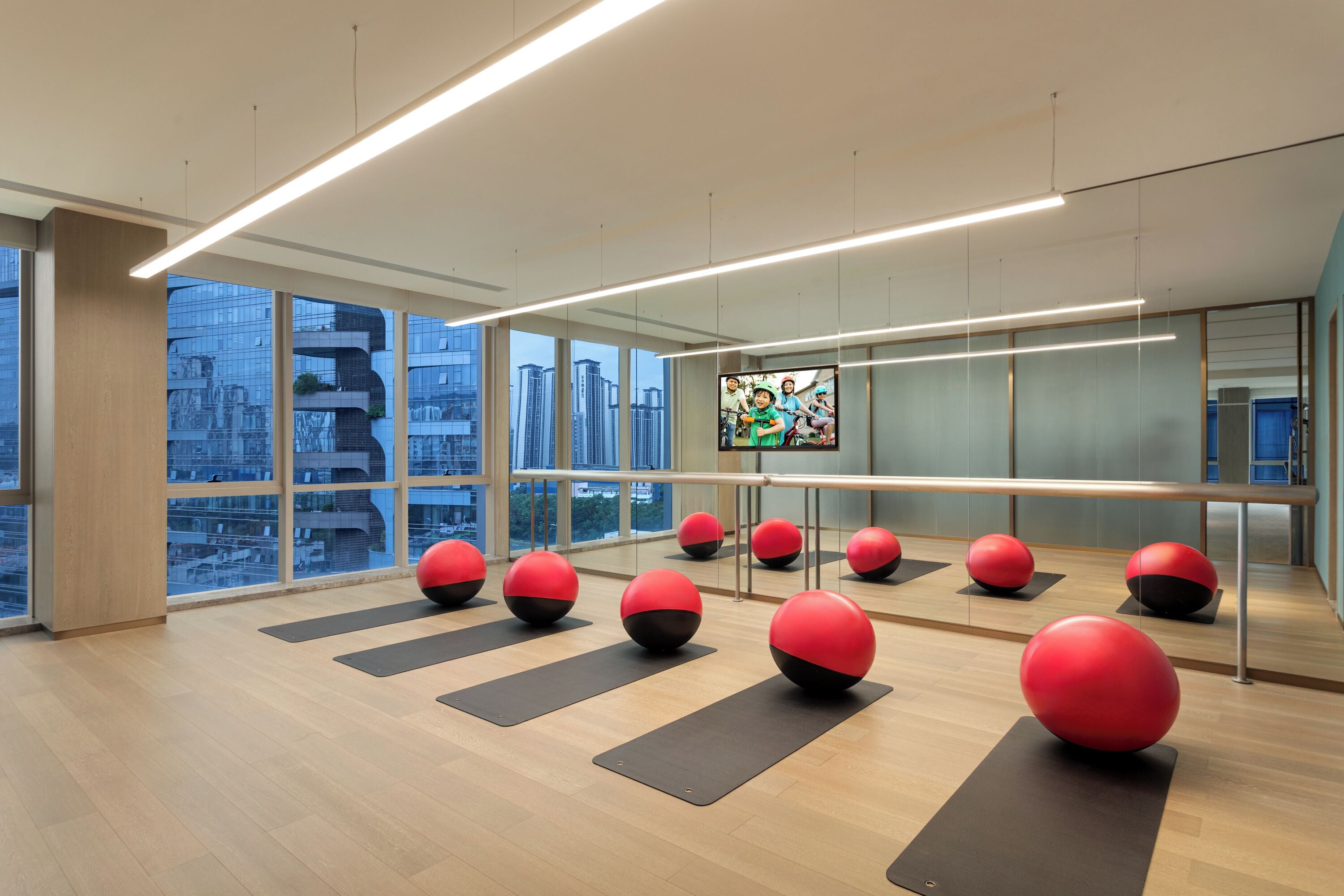 A modern fitness room with exercise balls and mats, large windows, and a city view.