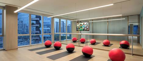A modern fitness room with exercise balls and mats, large windows, and a city view.