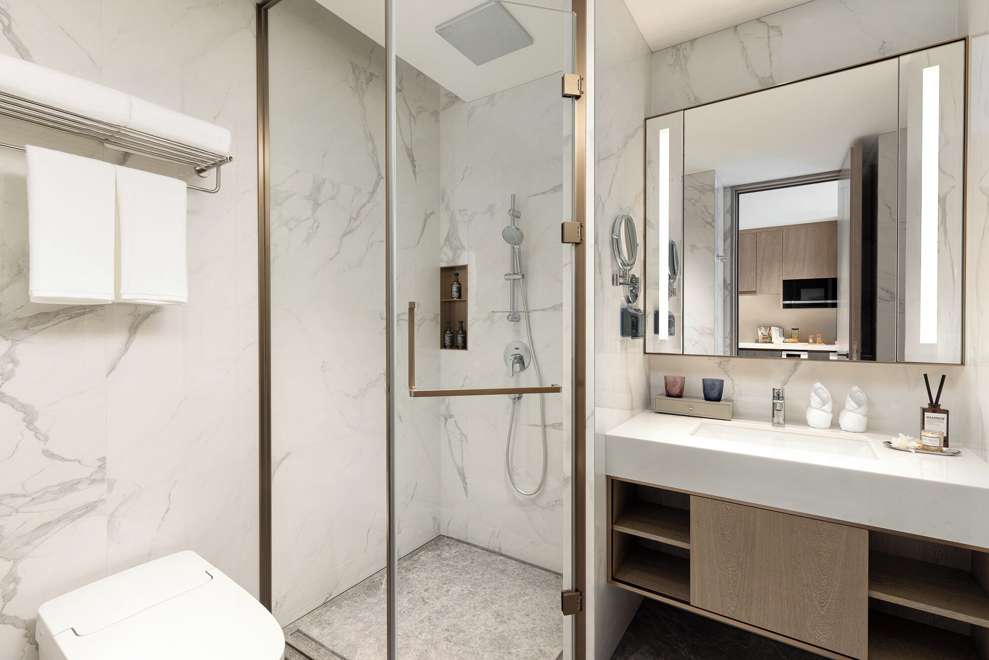 Une salle de bain moderne avec une douche à parois de verre, un lavabo blanc avec un grand miroir et des murs en marbre.