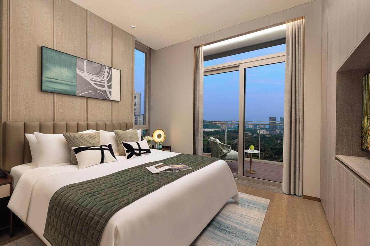 A modern hotel room with a large bed, a view of the city, and a balcony with a chair.
