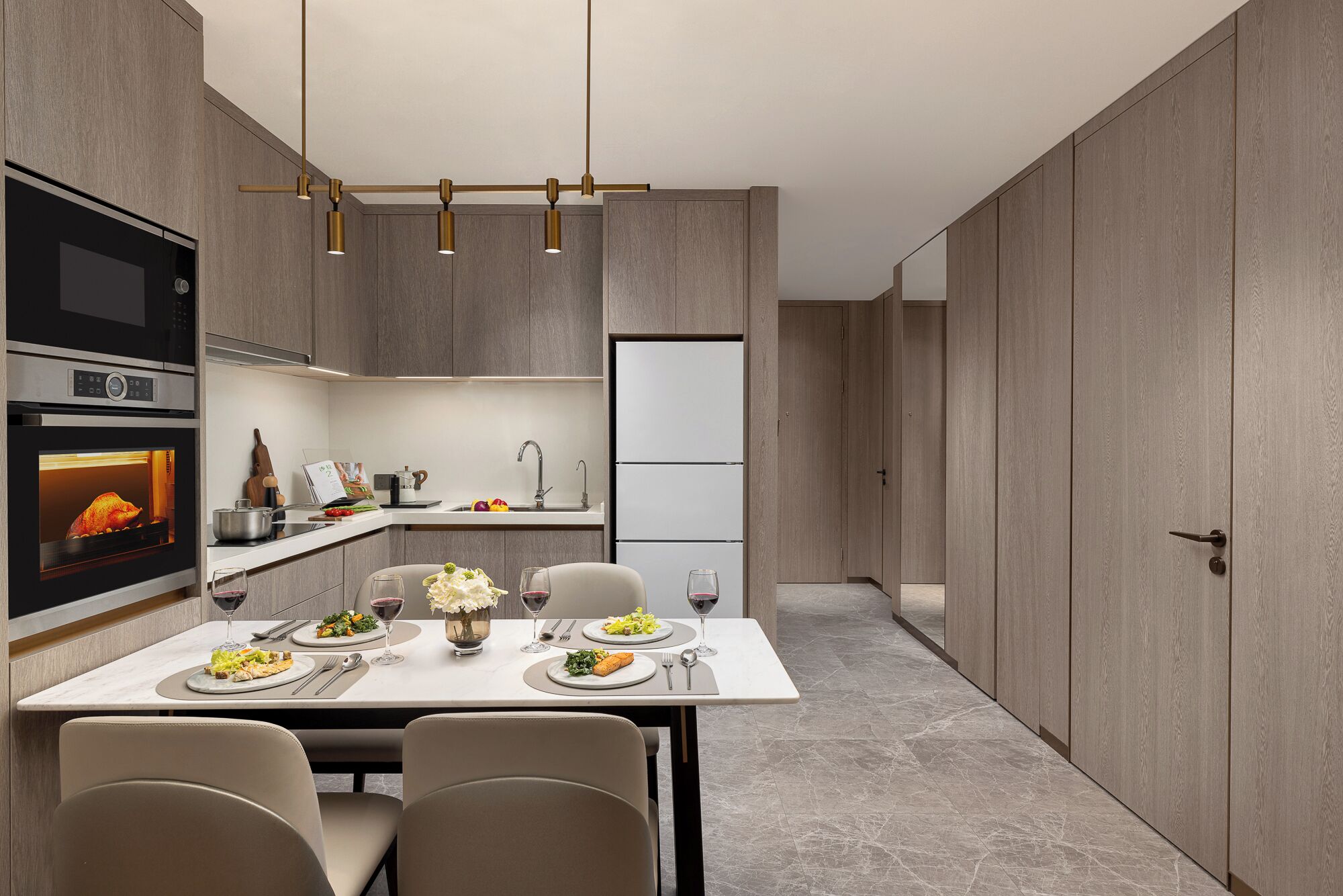 A modern kitchen with built-in appliances, a dining area with a table set for two, and a view into a hallway.