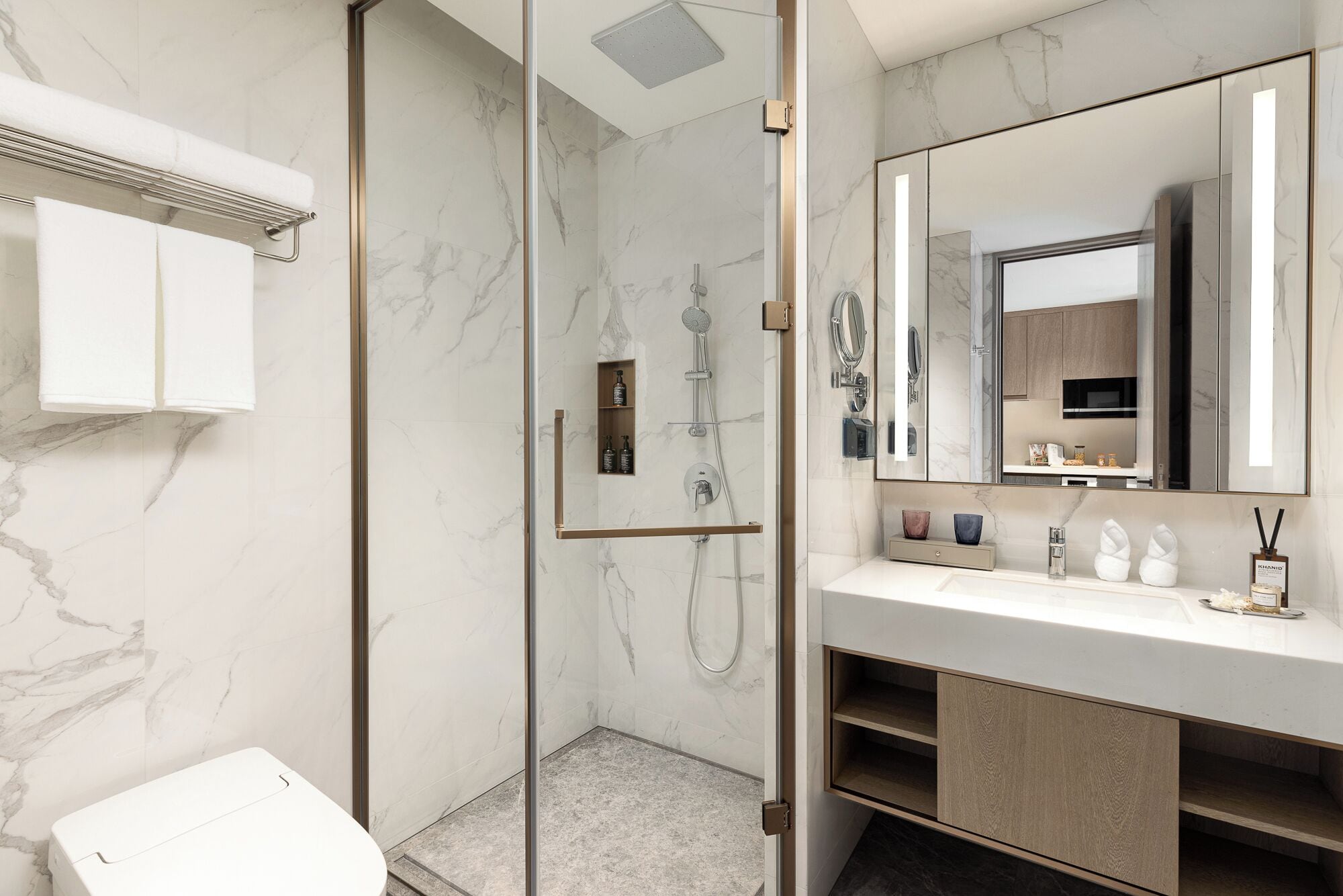 A modern bathroom with a glass-enclosed shower, a white sink with a large mirror, and marble walls.
