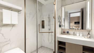 A modern bathroom with a glass-enclosed shower, a white sink with a large mirror, and marble walls.