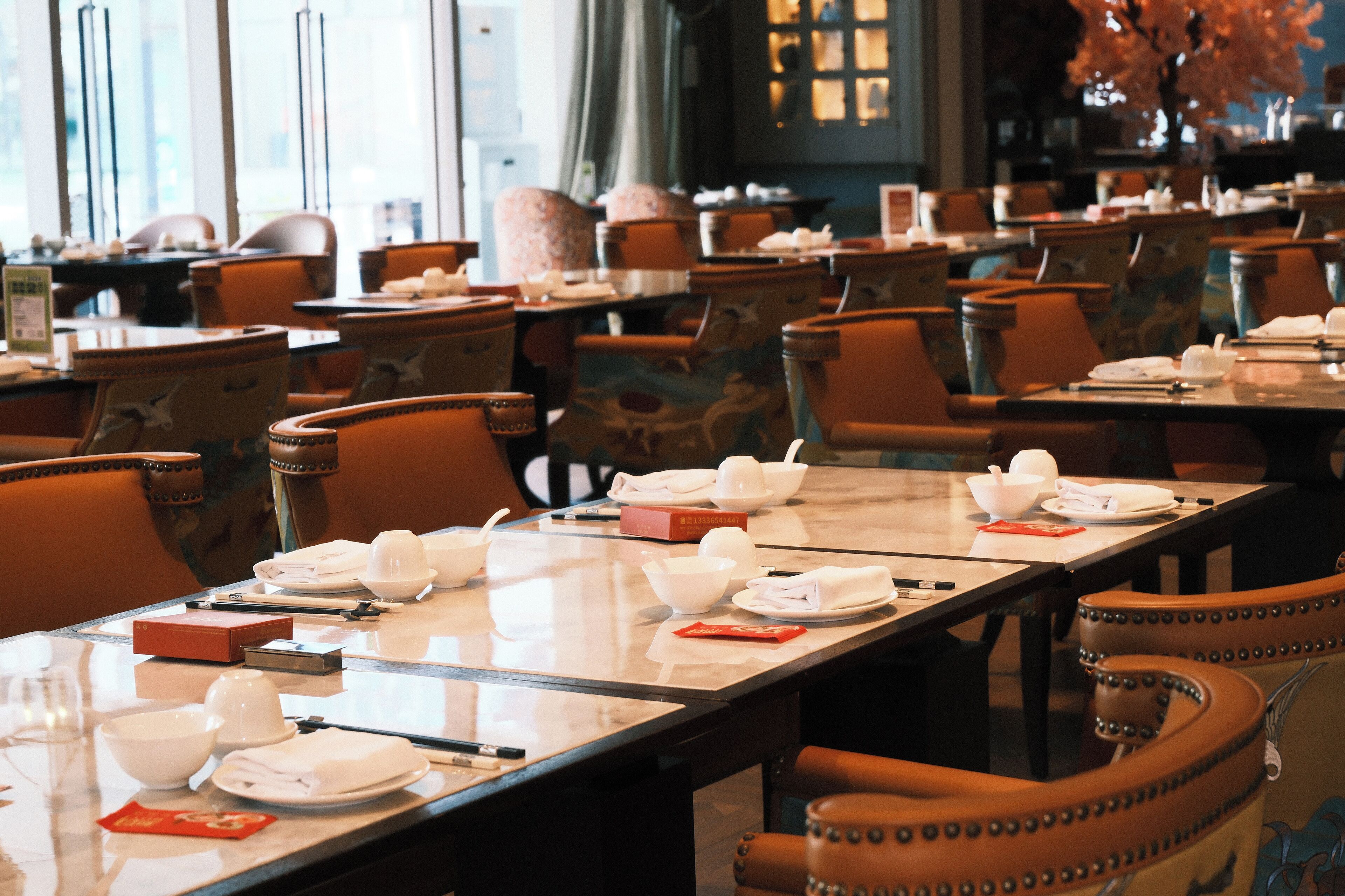 A restaurant with multiple tables set for dining, each with white bowls, plates, and napkins.
