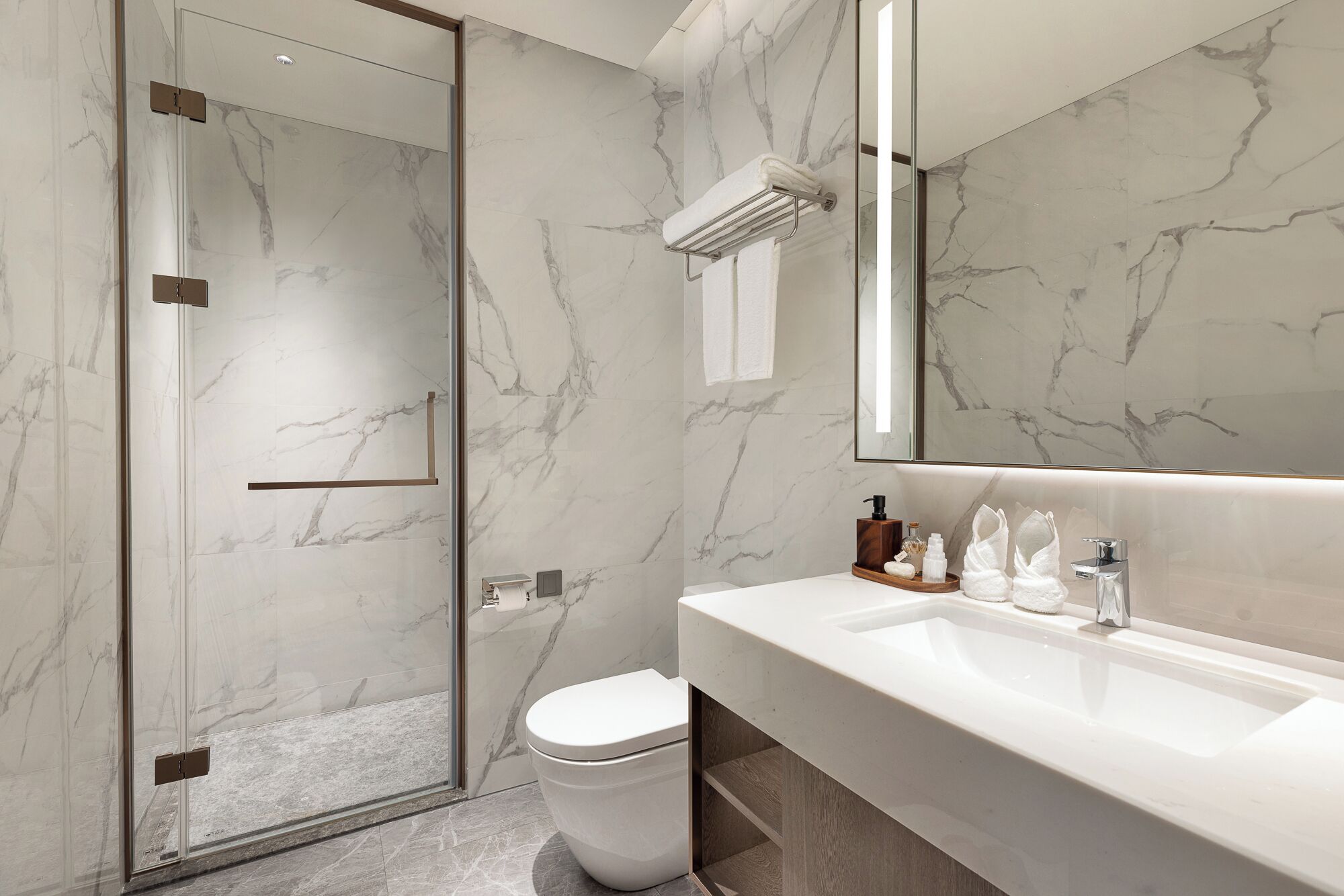 Un baño moderno con cabina de ducha de vidrio, un inodoro blanco y un lavamanos blanco con encimera de madera.