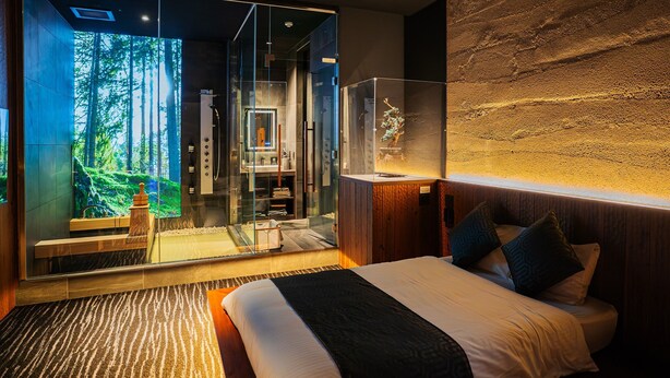 A modern bedroom with a large bed, a glass shower enclosure, and a view of a forest.