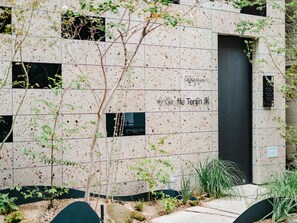 A building facade with a grid pattern, a black door, and some greenery in front. - Giraffe Tenjin Tsune (Fukuoka)